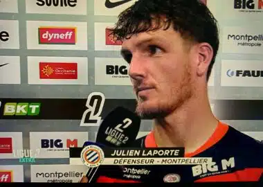 Football player Julien Laporte being interviewed after a match, holding a microphone in front of sponsor boards
