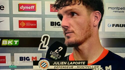 Football player Julien Laporte being interviewed after a match, holding a microphone in front of sponsor boards