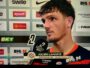 Football player Julien Laporte being interviewed after a match, holding a microphone in front of sponsor boards