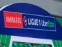 Signboard on a blue stadium arch reading 'BARRAGES' and 'LIGUE 1 Uber Eats' with red and green highlights