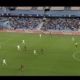 Soccer match in progress at a stadium; white and red teams vie for the ball near the right flank as the crowd watches, scoreboard shows MHSC 0-0 GF38 and 22:17.