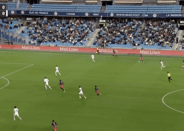 Soccer match in progress at a stadium; white and red teams vie for the ball near the right flank as the crowd watches, scoreboard shows MHSC 0-0 GF38 and 22:17.