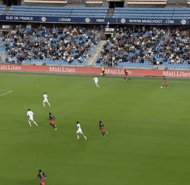 Soccer match in progress at a stadium; white and red teams vie for the ball near the right flank as the crowd watches, scoreboard shows MHSC 0-0 GF38 and 22:17.