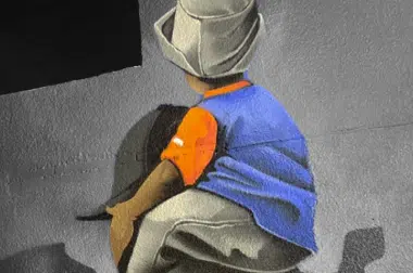 Back view of a person in a blue shirt and orange glove crouching against a gray wall, possibly painting graffiti on a mural.