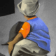 Back view of a person in a blue shirt and orange glove crouching against a gray wall, possibly painting graffiti on a mural.