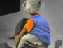 Back view of a person in a blue shirt and orange glove crouching against a gray wall, possibly painting graffiti on a mural.