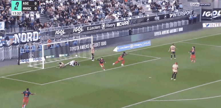 Soccer scene near goal: players in tan and red uniforms around the net as a ball sits by the goalkeeper on the ground, crowd in stands behind. BeIN SPORTS watermark visible.