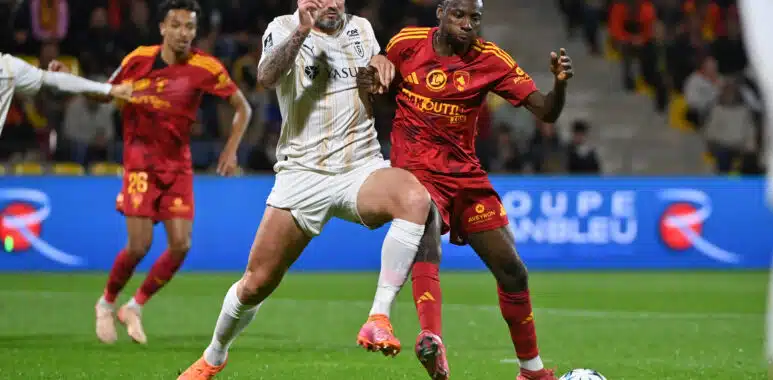 Two soccer players battle for the ball during a match, crowd watching in the stands behind them.