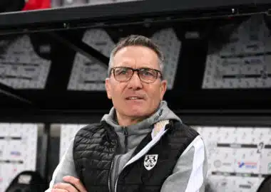 Man wearing glasses and a black puffer vest stands in front of a wall of boxes in a warehouse.**0