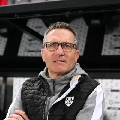 Man wearing glasses and a black puffer vest stands in front of a wall of boxes in a warehouse.**0