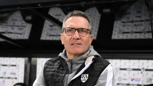 Man wearing glasses and a black puffer vest stands in front of a wall of boxes in a warehouse.**0