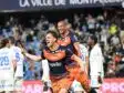 Two soccer players in orange and navy rush of celebration on the field as fans applaud in the stands, one pointing joyfully