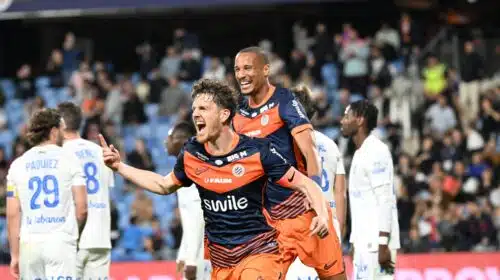 Two soccer players in orange and navy rush of celebration on the field as fans applaud in the stands, one pointing joyfully