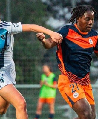 Two female soccer players race for the ball on a grass field during a match, one in white with blue stripes and the other in orange and navy.
