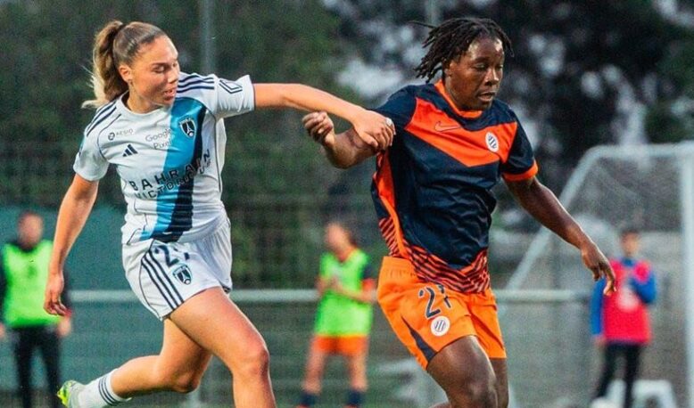 Two female soccer players race for the ball on a grass field during a match, one in white with blue stripes and the other in orange and navy.