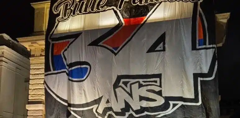 Nighttime street view: a large white banner with bold black outline '34' and colorful red/blue accents covering a building fa&ccedil;ade.