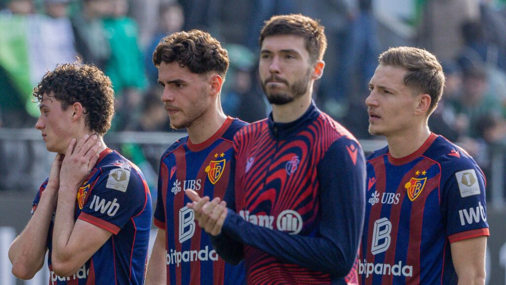 8666d7d2-8a15-4ab9-9fba-533f47388db5 | AllezPaillade.com Four football players in blue and red striped uniforms stand together on the field, hands at their sides or near their chests, with a blurred crowd in the background.
