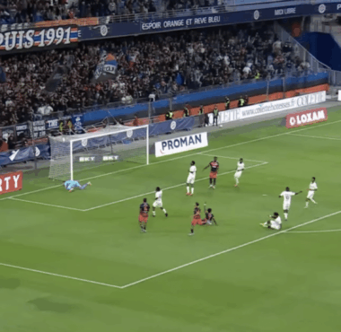 Soccer match; goalkeeper dives to stop a shot near the goal as attackers and defenders crowd the area.