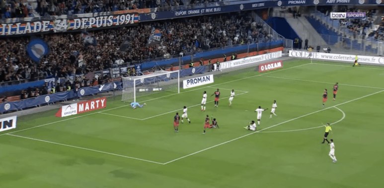 Soccer match; goalkeeper dives to stop a shot near the goal as attackers and defenders crowd the area.