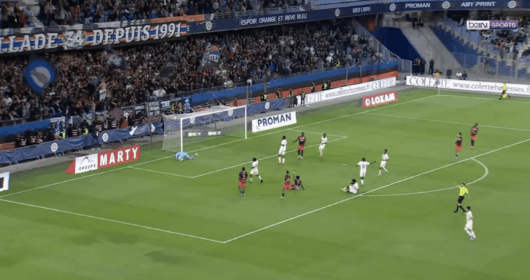 Soccer match; goalkeeper dives to stop a shot near the goal as attackers and defenders crowd the area.