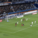 Soccer match; goalkeeper dives to stop a shot near the goal as attackers and defenders crowd the area.