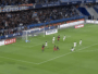 Soccer match; goalkeeper dives to stop a shot near the goal as attackers and defenders crowd the area.