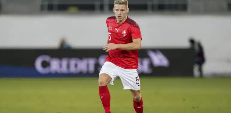 SCHWEIZ - KROATIEN | AllezPaillade.com Soccer player in a red jersey with number 5 dribbling the ball on a grass field; Swiss team crest visible on chest.
