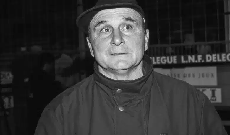 Black-and-white photo of a man in a fedora and high-collar coat, eyes wide in a startled expression.