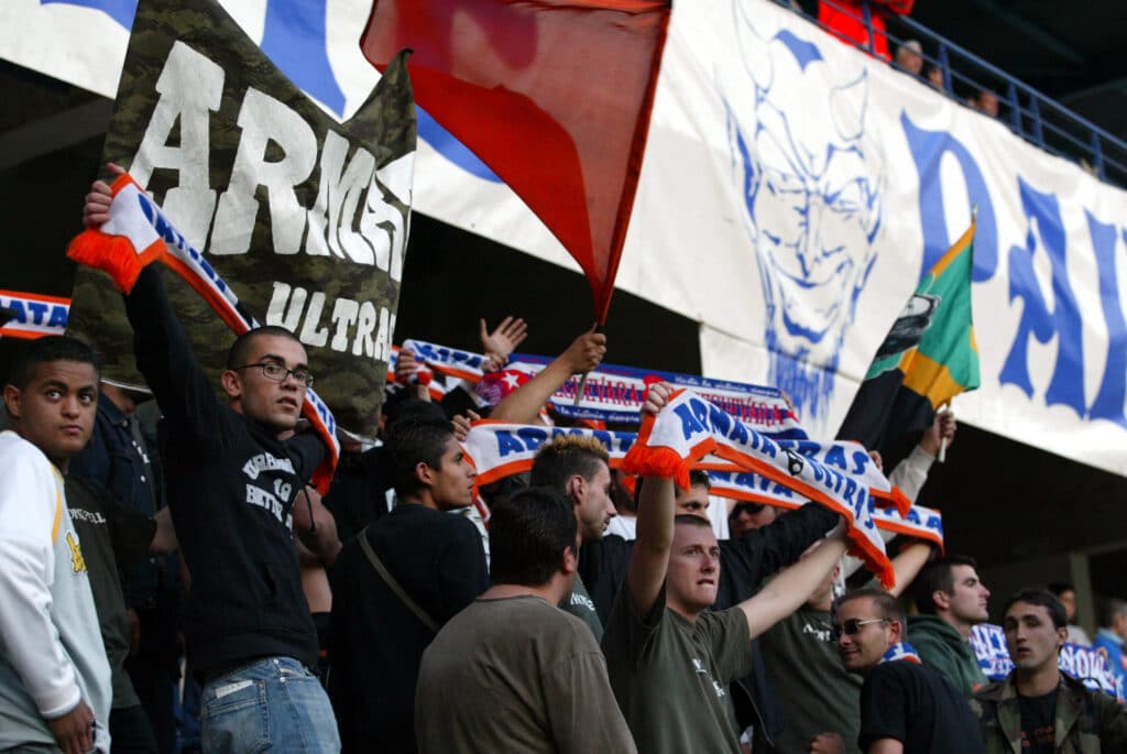 Crowd of sports fans in a stadium, waving orange, blue, and white scarves and banners.