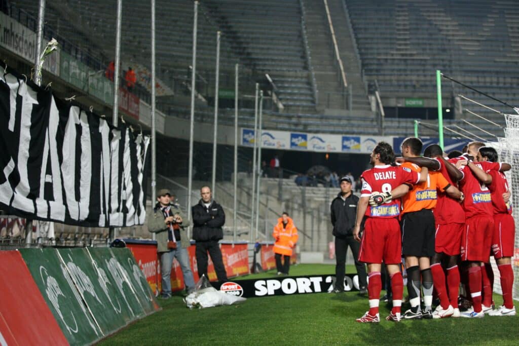 Soccer players in red jerseys huddle on the sideline of a stadium, celebrating together near the goal area.
