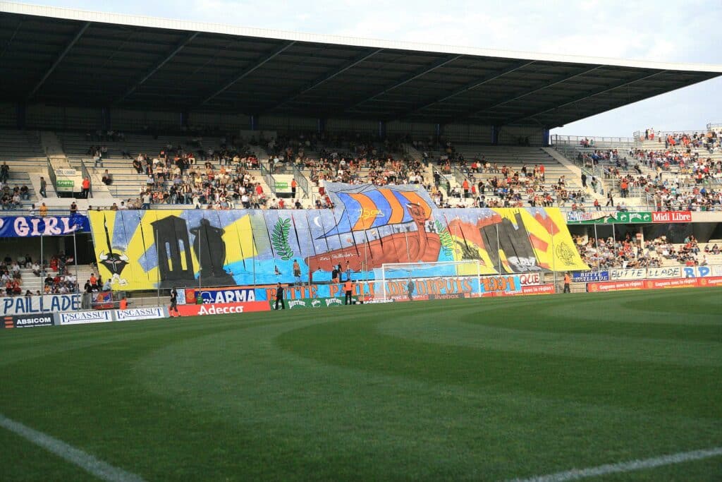 Crowd of spectators in a stadium stands with large colorful banners along the front, view from the field.