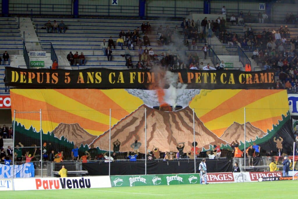 Large black banner with yellow text across a stadium, above a colorful mountain mural and cheering fans in the stands.