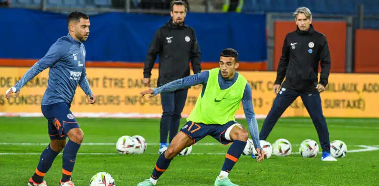 Savanier Sainte-Luce Montpellier Herault Sport Club v Olympique Gymnaste Club Nice - Ligue 1 Uber Eats | AllezPaillade.com Soccer players train on a grass field, dribbling and passing with multiple balls; foreground player in a neon vest controls the ball.