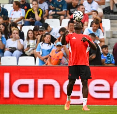Soccer player in red jersey heads the ball with crowds watching in the stands behind.