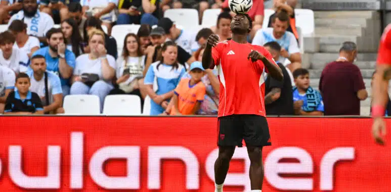 Soccer player in red jersey heads the ball with crowds watching in the stands behind.