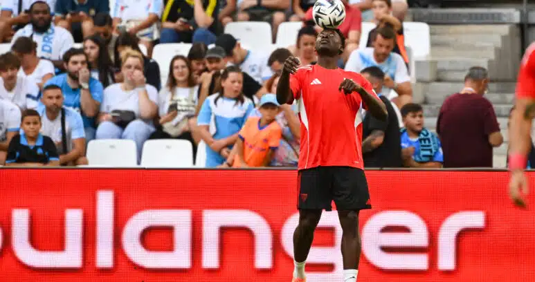 Soccer player in red jersey heads the ball with crowds watching in the stands behind.