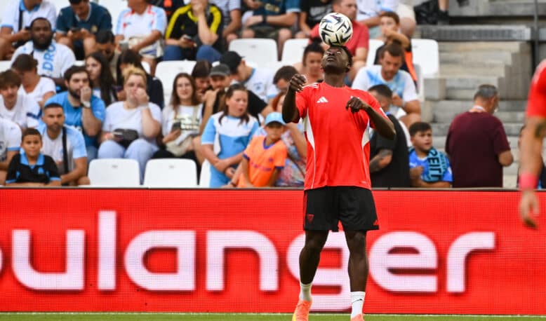 Soccer player in red jersey heads the ball with crowds watching in the stands behind.