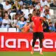 Soccer player in red jersey heads the ball with crowds watching in the stands behind.