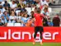 Soccer player in red jersey heads the ball with crowds watching in the stands behind.