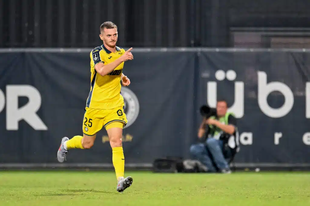 Soccer player in a yellow kit running on the field, pointing forward with his right hand during a match.