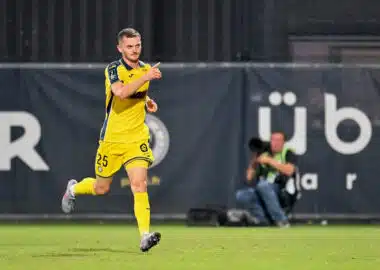 Soccer player in a yellow kit running on the field, pointing forward with his right hand during a match.