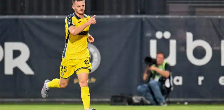 Soccer player in a yellow kit running on the field, pointing forward with his right hand during a match.