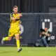 Soccer player in a yellow kit running on the field, pointing forward with his right hand during a match.
