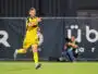 Soccer player in a yellow kit running on the field, pointing forward with his right hand during a match.