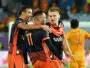 Soccer players in navy and orange jerseys celebrate with a group hug on the field.