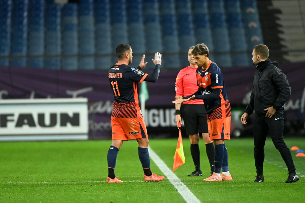 Soccer players in orange and navy uniforms high-five near the sideline during a match, with a referee and coach nearby.