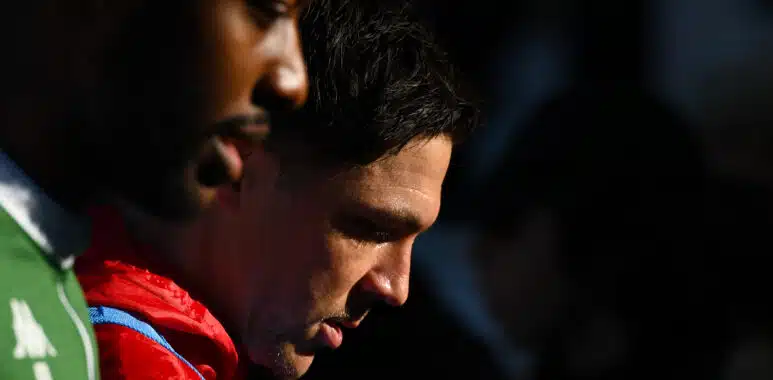 Red Star 93 v US Boulogne - Ligue 2 BKT 20252026 | AllezPaillade.com Two athletes standing close with heads bowed; one in a red jacket and the other in a green bib, against a dark background.