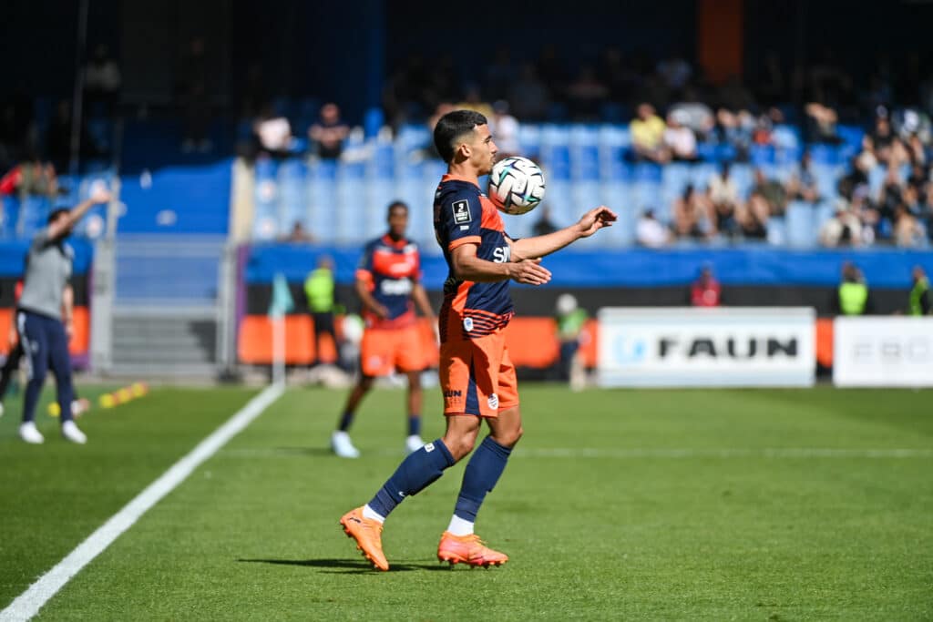 Sainte-Luce Montpellier Herault SC v ESTAC Troyes - Ligue 2 BKT 20252026 | AllezPaillade.com Soccer player in orange-blue kit controls a ball mid-air on a green pitch with blurred spectators in the stands behind him.