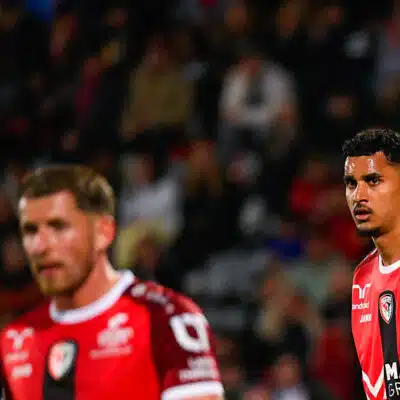 Two soccer players in red jerseys on the field during a match, one wearing a yellow captain's armband, focused on the game.