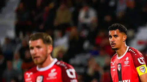 Two soccer players in red jerseys on the field during a match, one wearing a yellow captain's armband, focused on the game.